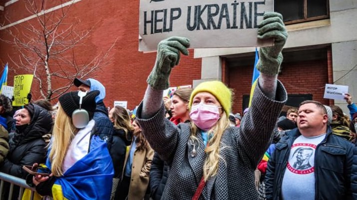 Mulher segura um cartaz escrito em inglês Stop War em meio a manifestantes com bandeira da Ucrânia | Rússia