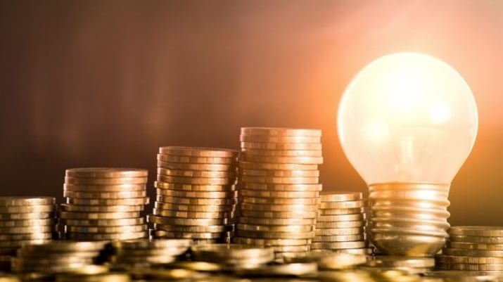Imagem mostrando pilhas de moedas cada vez maiores, com uma lâmpada acesa à direita. Simboliza a alta da Selic e dos juros e as ideias de investimento em renda fixa e renda variável nesse cenário