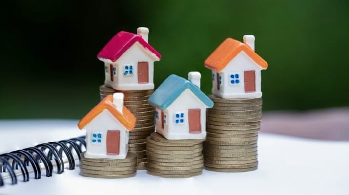 Imagem mostra pequenas casas de brinquedo sobre pilhas de moedas, representando os dividendos pagos mensalmente pelos fundos imobiliários (FIIs) | fundo imobiliário HGLG11