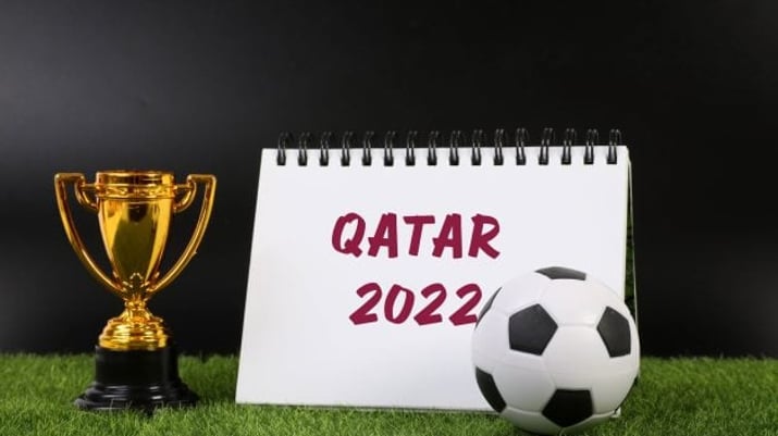 Taça dourada, calendário escrito Catar 2022 e uma bola de futebol sobre o gramado; jogos do Brasil Copa 2022