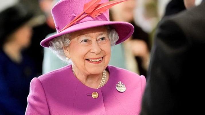 Foto de meio corpo da rainha Elizabeth II, vestindo roupas roxas e de chapéu com pena