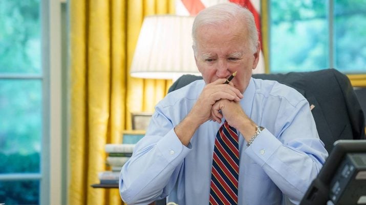 O presidente dos EUA, Joe Biden, sentado e apoiado em uma mesa, com uma caneta na mão, pensativo