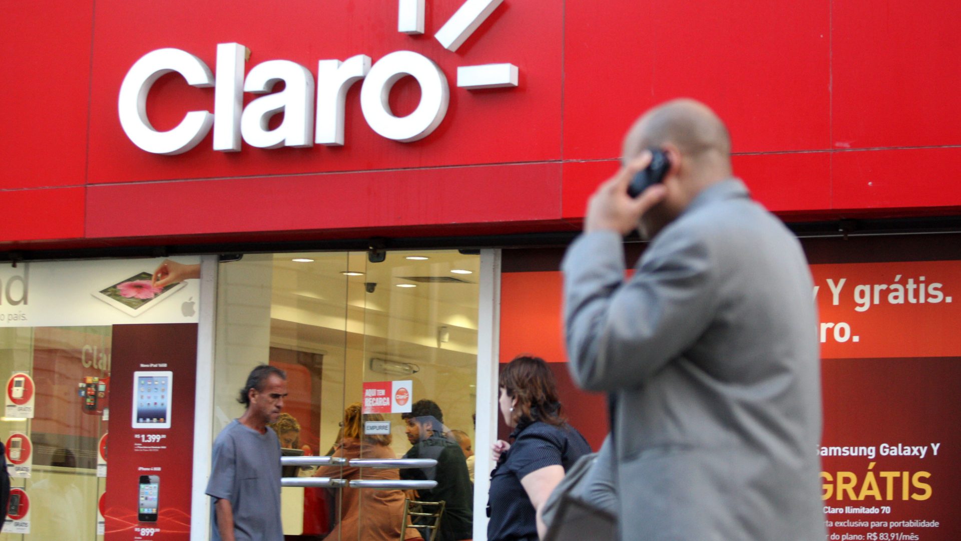 Homem usando celular caminha próximo à fachada de loja da operadora Claro, no centro do Rio de Janeiro.