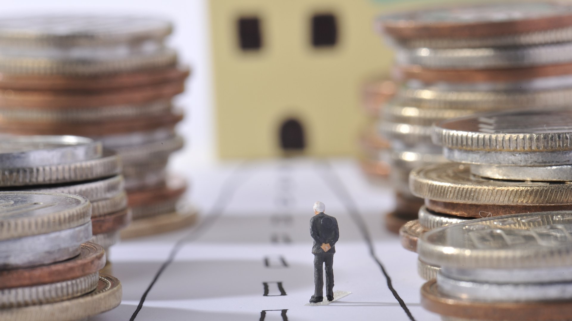 Imagem traz miniatura de idoso ao lado de pilhas de moedas