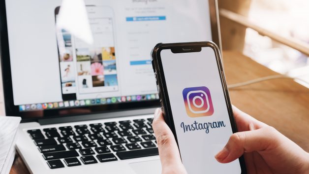 Imagem de celular com logo do Instagram na tela sendo segurado por duas mãos