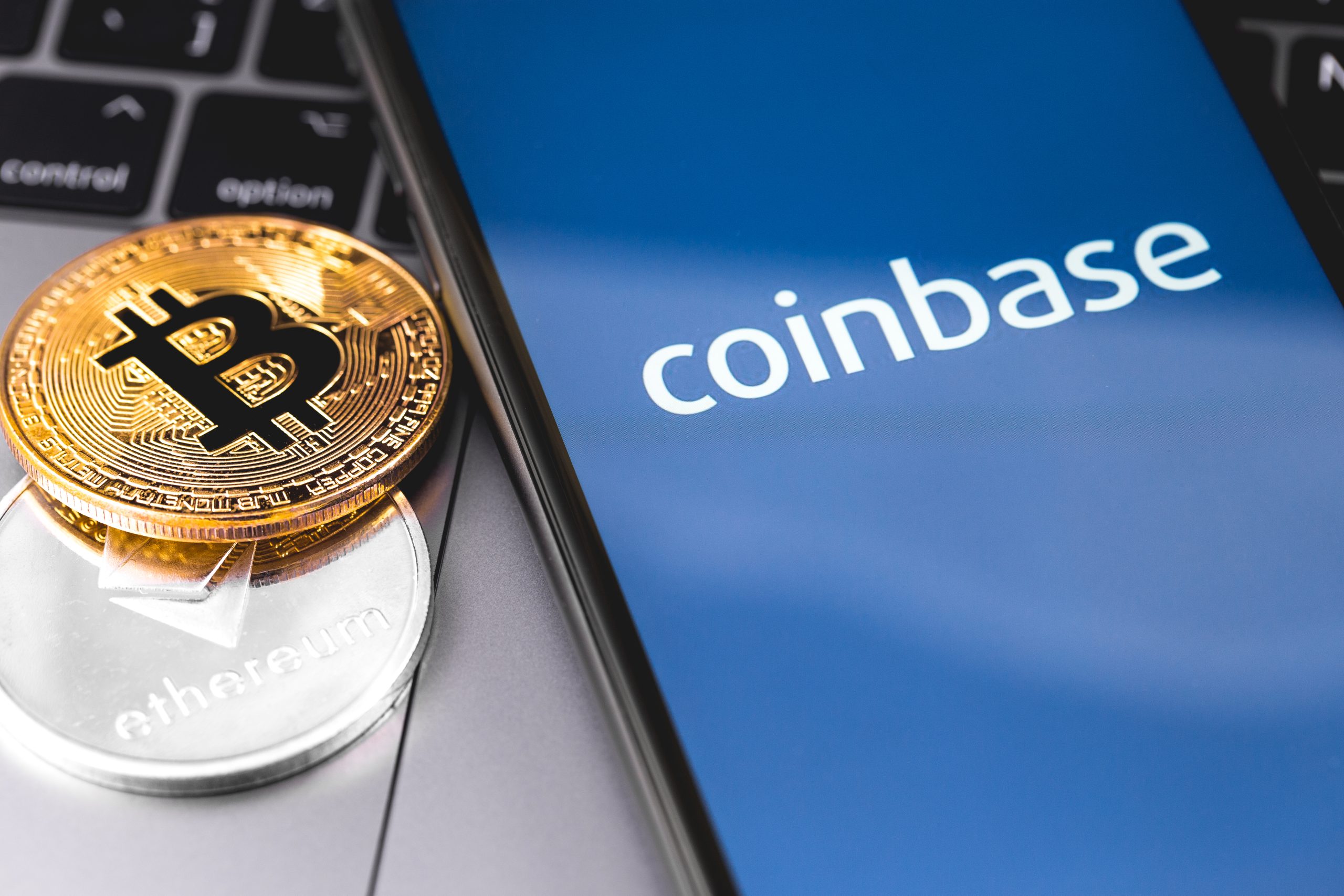 Logo da exchange Coinbase em tela de celular ao lado do símbolo do bitcoin