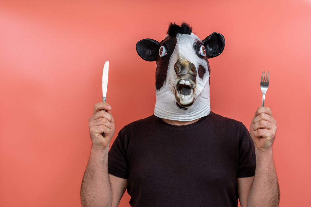 Pessoa vestida com uma máscara de vaca segurando um garfo e uma faca nas mãos