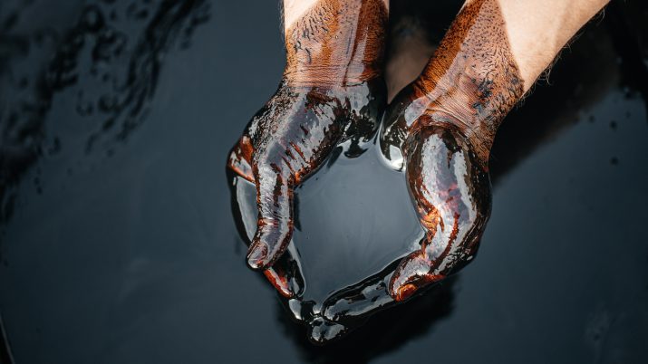 Mãos em concha segurando um líquido escuro, parecido com petróleo