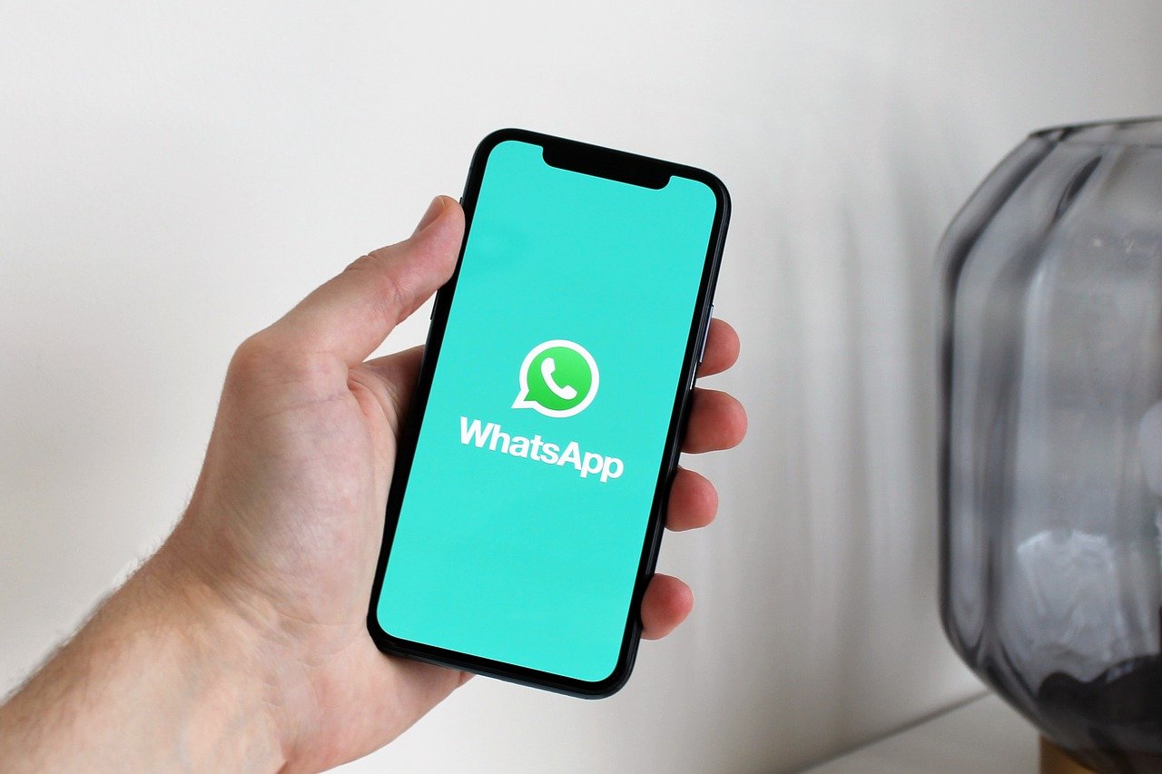 Mão segurando celular com tela no WhatsApp. Fundo branco.