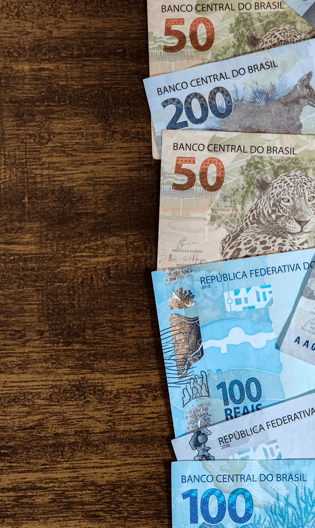 Notas de 50, 100 e 200 reais sobre fundo de madeira
