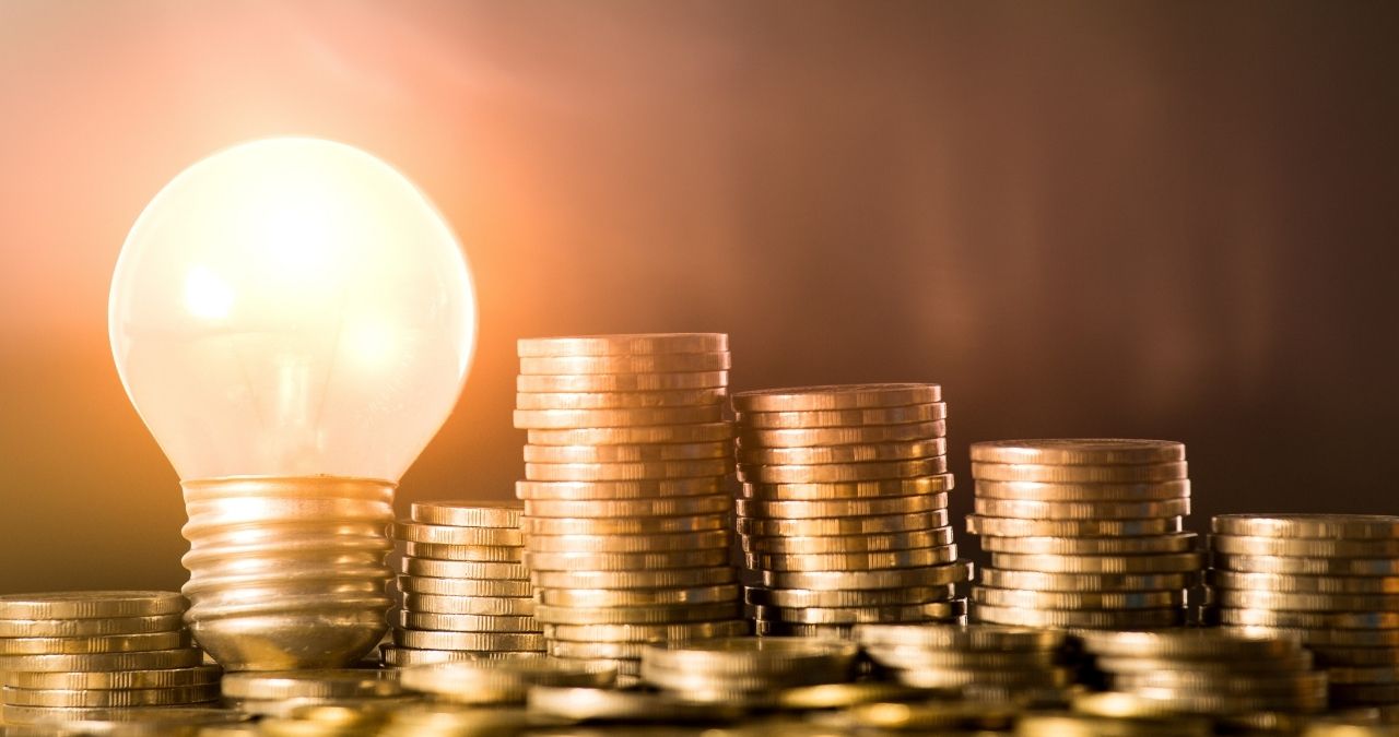 Lâmpada ao lado de moedas empilhadas, representando renda fixa