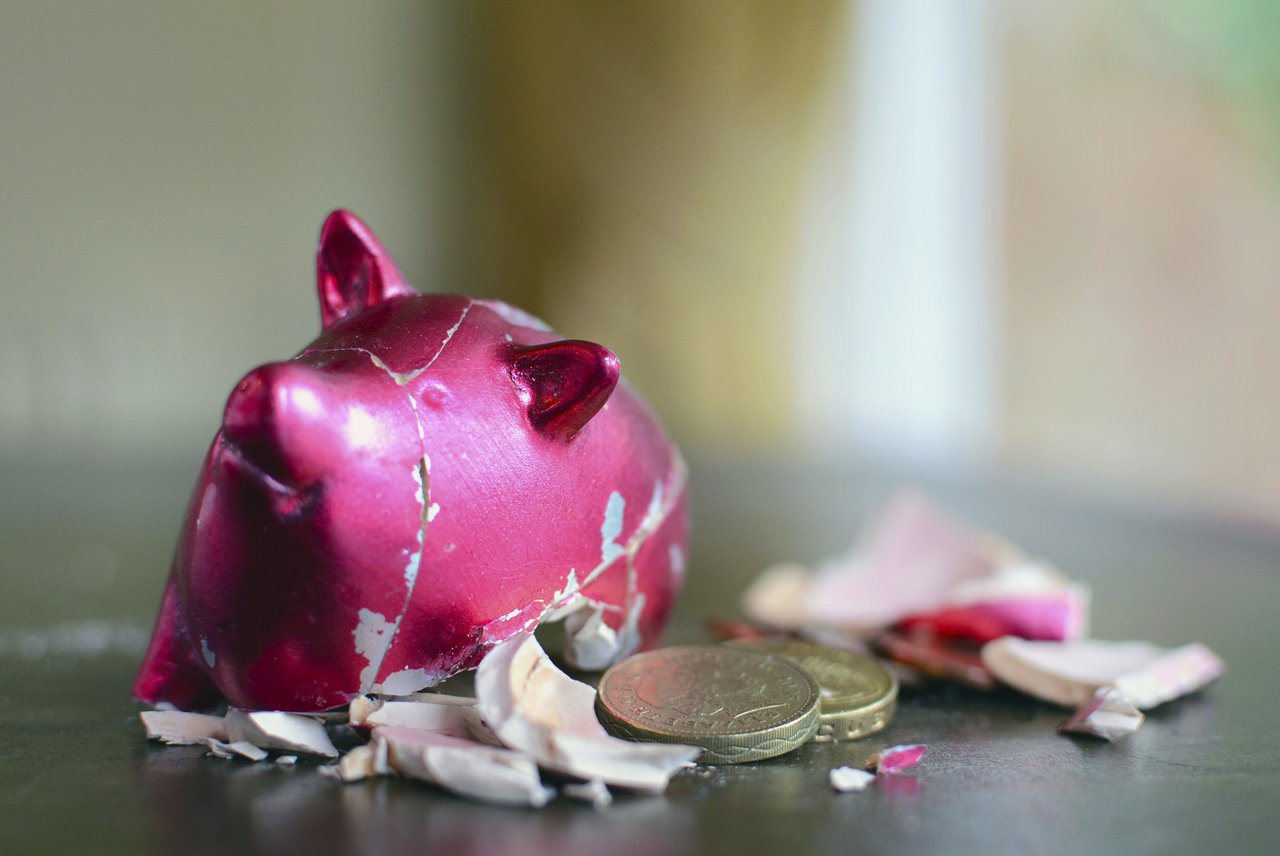 Cofrinho cor de rosa em formato de porco esmagado e com moedas caídas para fora | Poupança
