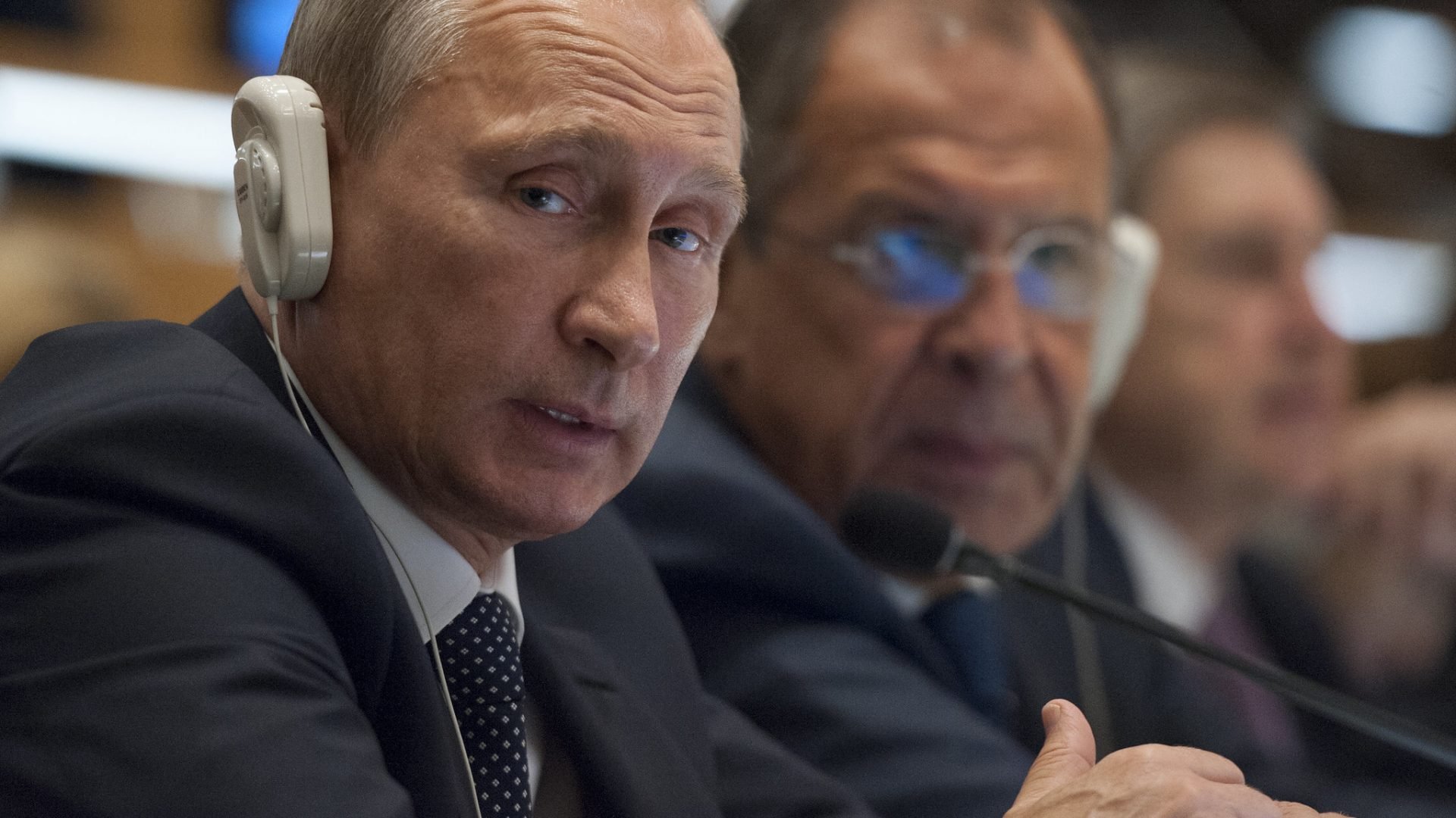 Presidente russo, Vladimir Putin, sentado em uma mesa com fone ouvido