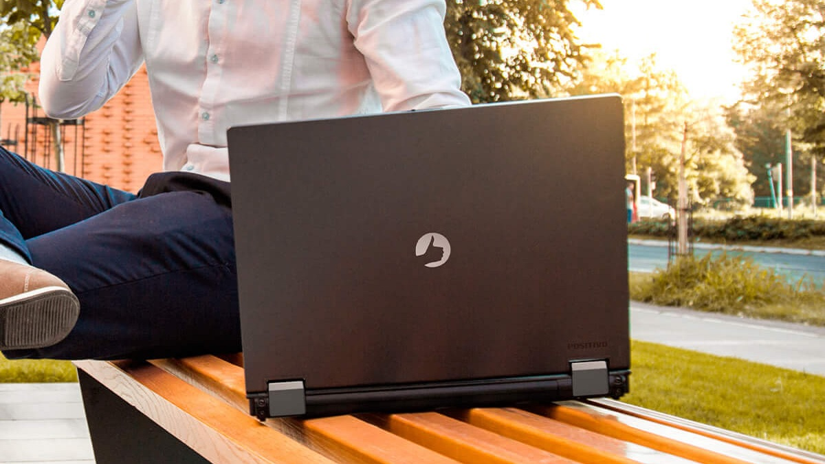 Homem sentado em um banco de praça com um notebook da Positivo
