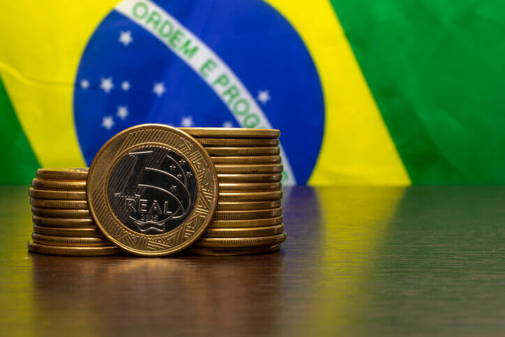 Moedas de real com bandeira do Brasil ao fundo