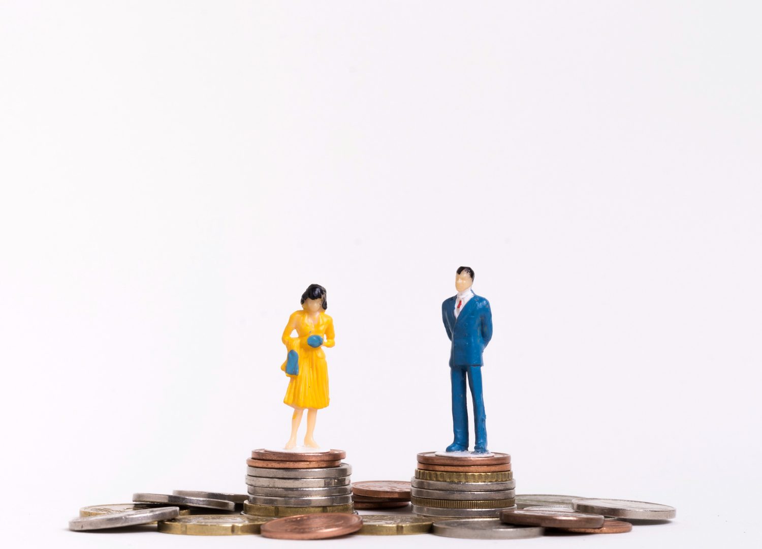homem com terno azul e mulher de vestido amarelo, ambos em pé, cada um sobre uma torre de moedas representando a igualdade salarial