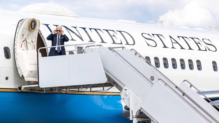 O presidente dos EUA, Joe Biden, aparece de pé, na porta do avião Air Force 1, colando óculos escuros