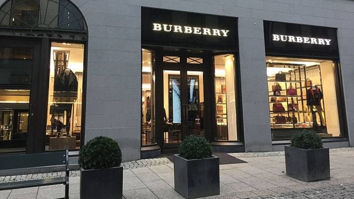 Fachada de uma loja da Burberry em Oslo, com arranjos de plantas na frente, um banco do lado esquerdo e o letreiro iluminado