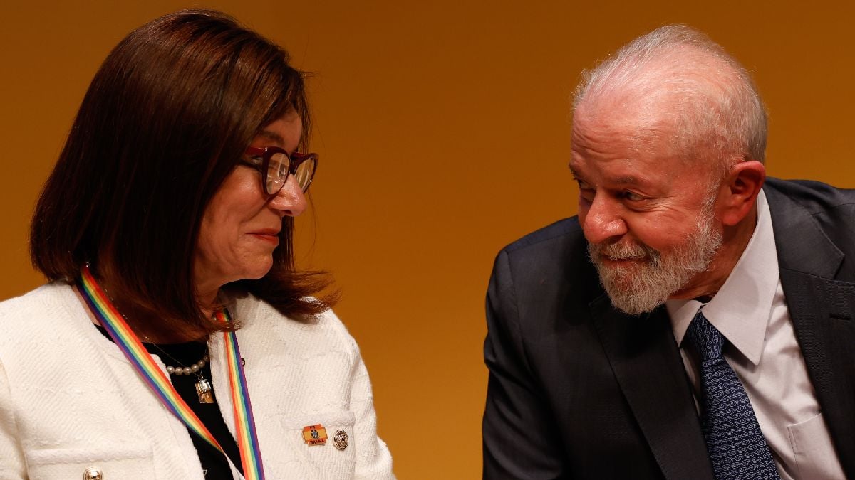 Magda Chambriard à esquerda da imagem, sorrindo e olhando em direção ao presidente do Brasil, Luiz Inácio Lula da Silva, que está à direita da imagem. Lula também olha para Magda sorrindo.