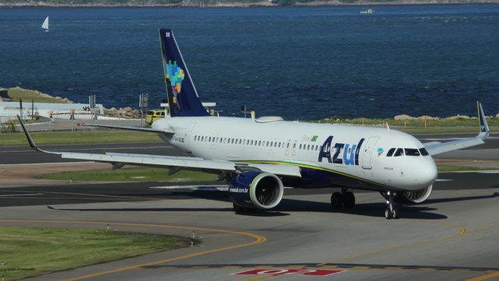 Aeronave branco e azul escuro em pista, com mar ao fundo. O avião é da companhia de aviação Azul