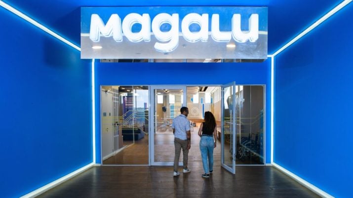 Fachada da Arena Magalu, em São Paulo. Paredes azuis e placa na parte superior com os dizeres "Magalu" em led branco. Portas transparentes com duas pessoas entrando