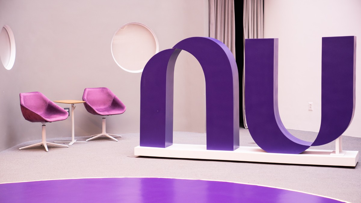 Ambiente com duas cadeiras roxas na lateral e símbolo do Nubank no centro