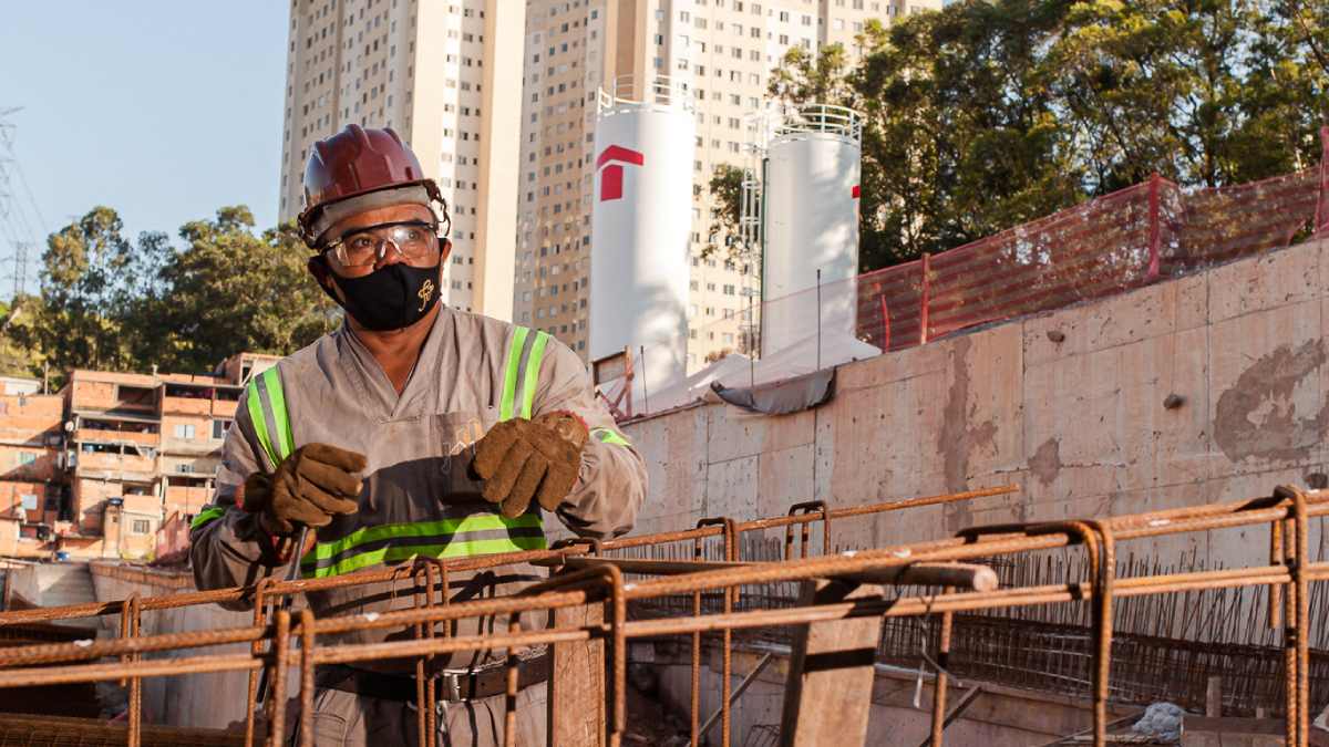 Técnico de construção no primeiro plano. Atrás, duas torres com símbolo vermelho da Tenda e prédios.
