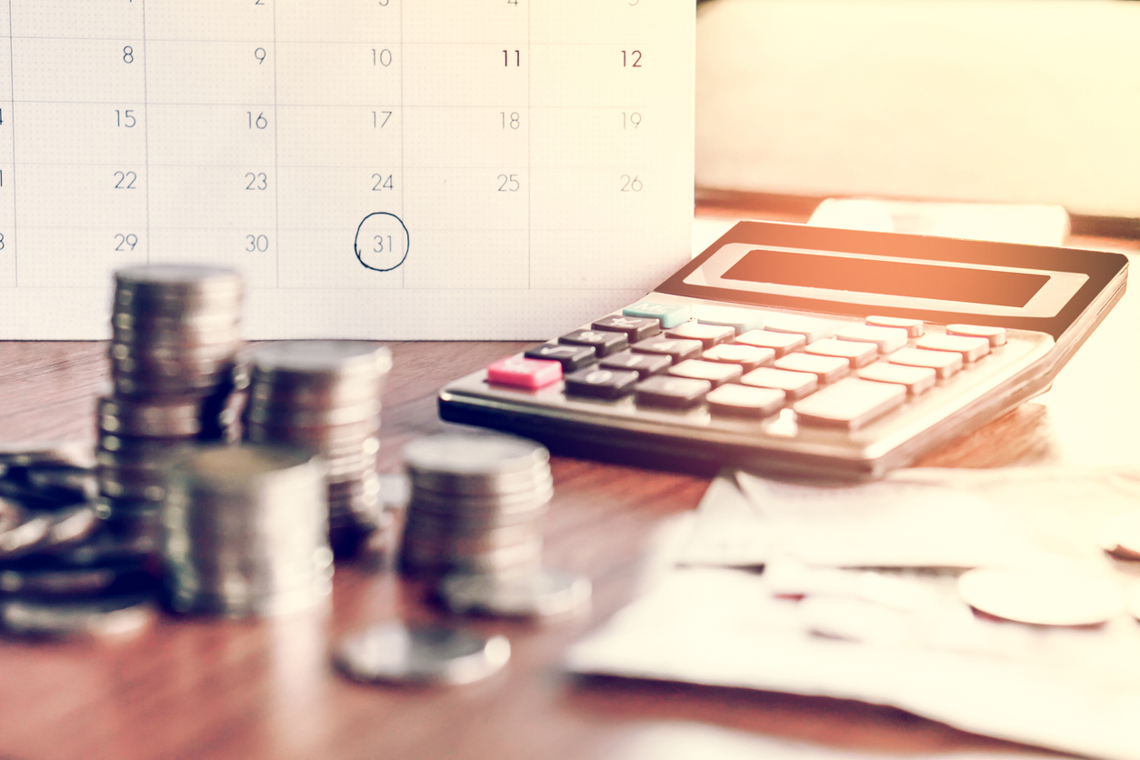 Calendário com o foco nas datas do fim do mês e com o dia 31 circulado. Há moedas, papéis e calculadora sobre uma mesa