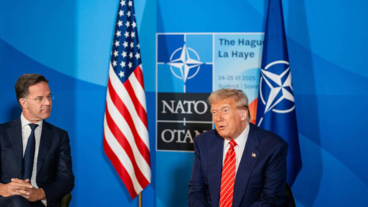 Imagem mostra Donald Trump vestindo terno azul e gravata vermelha. Ele está sentando em uma cadeira ao lado do presidente da Otan, Mark Rutte, que também usa terno escuro e camisa branca. De fundo, a bandeira dos EUA e o símbolo da Otan.