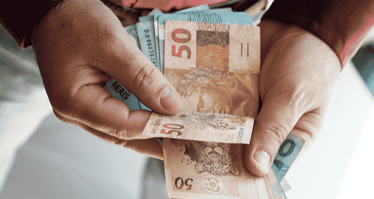 Mãos segurando diversas notas de cinquenta reais.